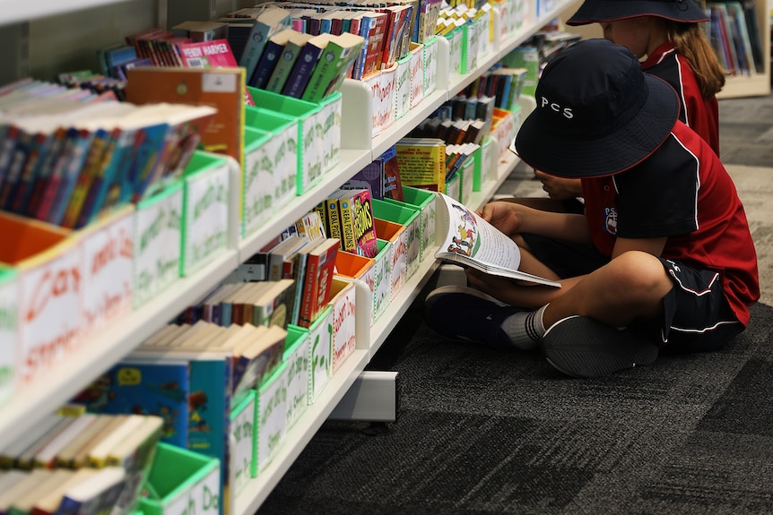 primary students sit onthne ground at Penrith Christian School reading a book