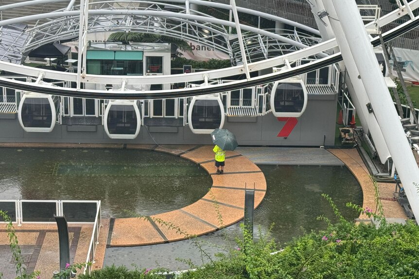 A man with an umbrella stands outside of the Wheel of Brisbane.