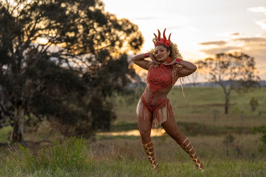 An elaborately dressed dancer stands posed on a hill.