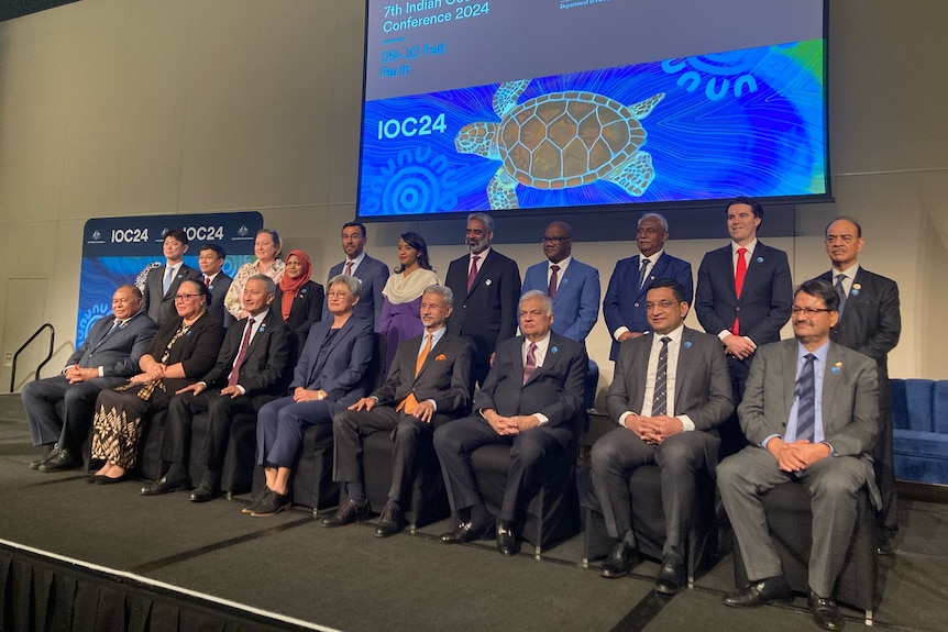 Men and women wearing suits sit in two rows for a photo. 