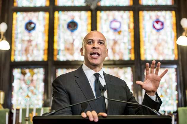 Cory Booker speaks to a crowd, backlit by golden light from stained-glass windows.