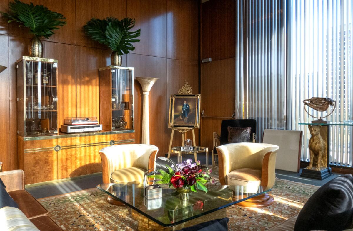 A Late Modern room with large windows features a glass coffee table, a replica of "Blue Boy" and tropical plants.