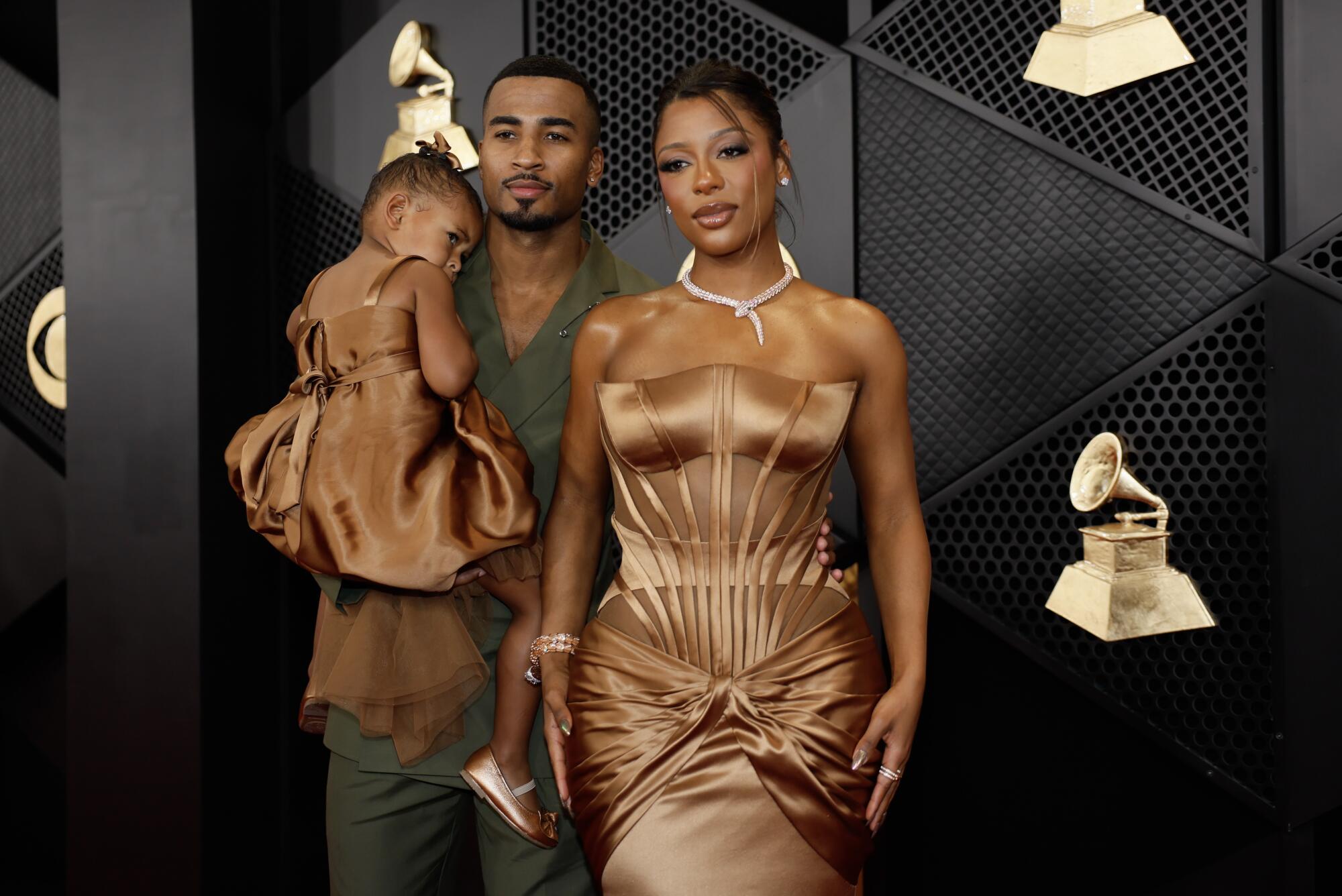 A woman in a bronze dress on the red carpet with a man carrying a little girl