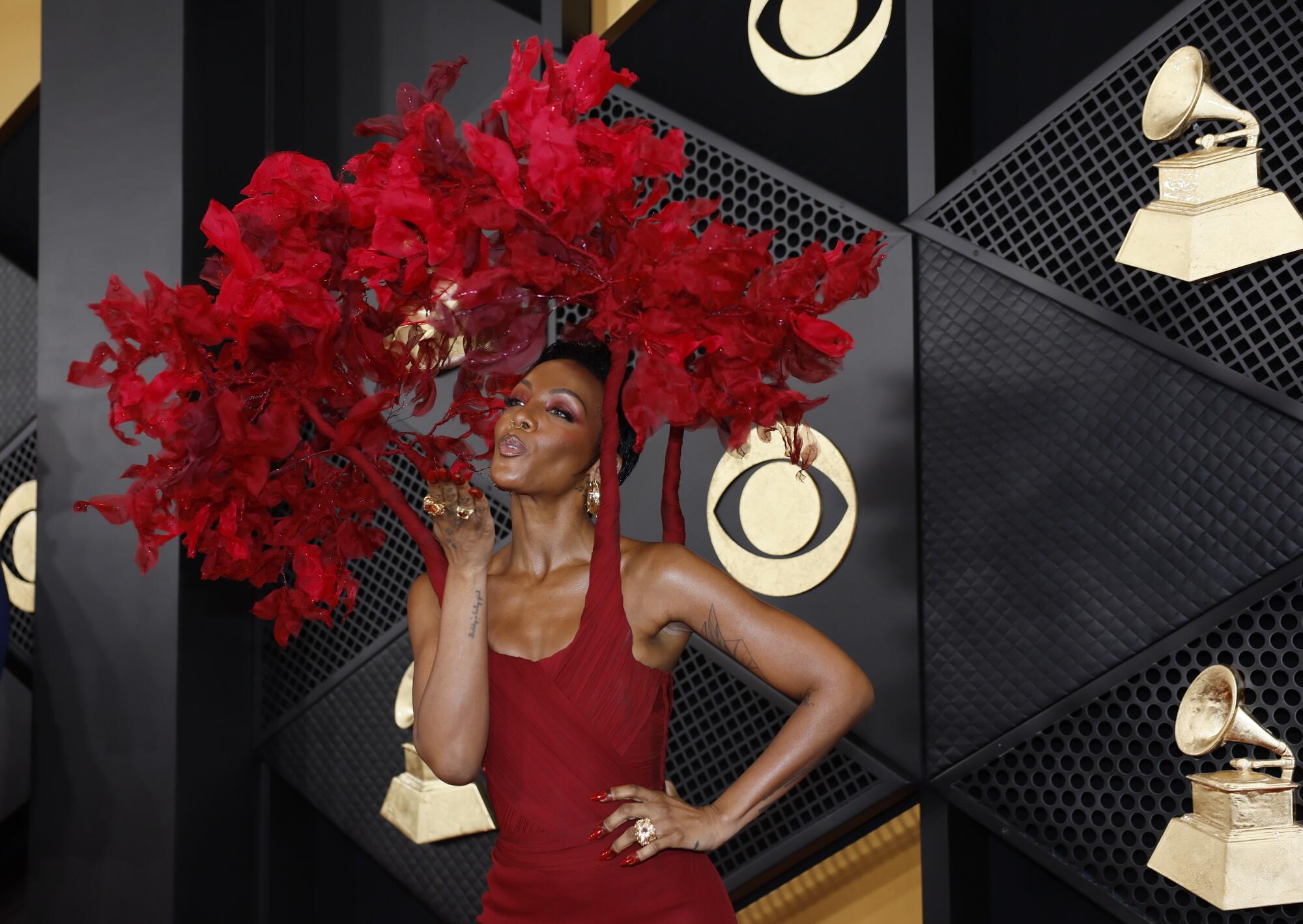 A woman blowing a kiss in a red dress that connects to an elaborate red floral headpiece