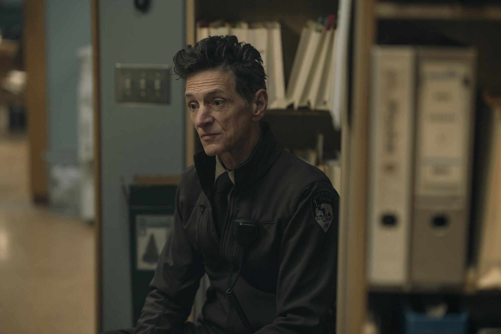 A police officer leans against shelves filled with files and binders.