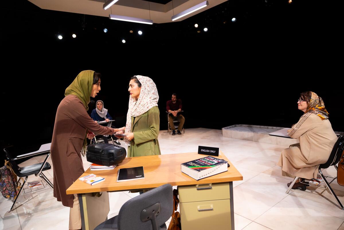 A group of actors on stage dressed as Iranian women, their heads wrapped in scarves, inhabit a clasroom set.