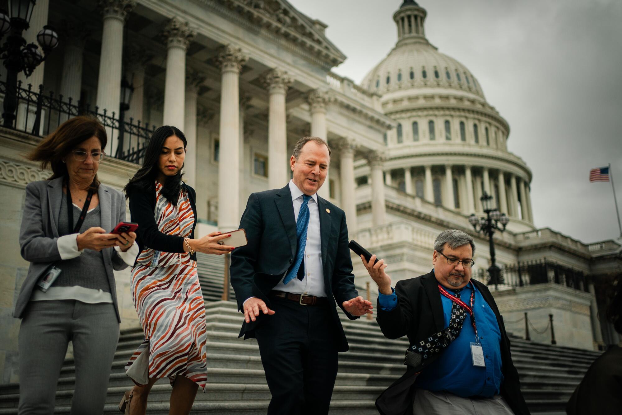 Adam Schiff talking as he walks down a stairway outside the Capitol with three reporters as they record him and take notes