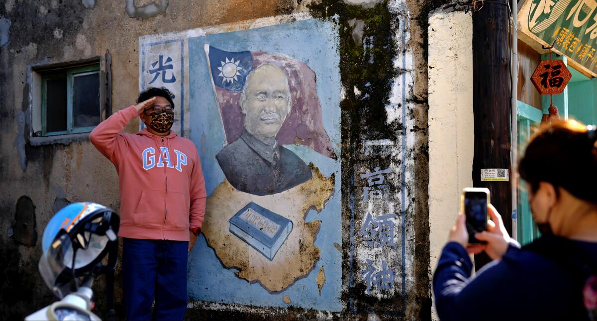 A young man salutes near a government poster as his photo is taken in "Island in Between." 