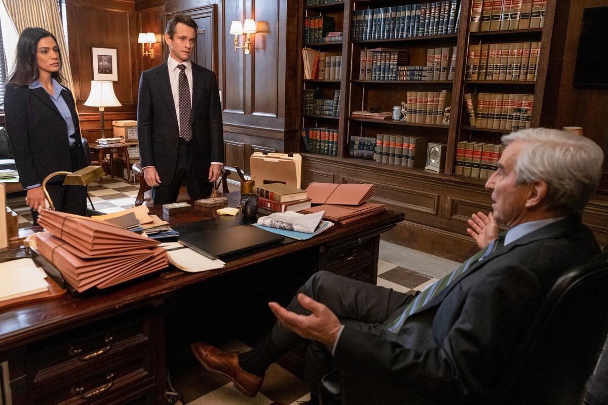 A woman and a man stand in front of a desk and a man in an office chair sits behind it.