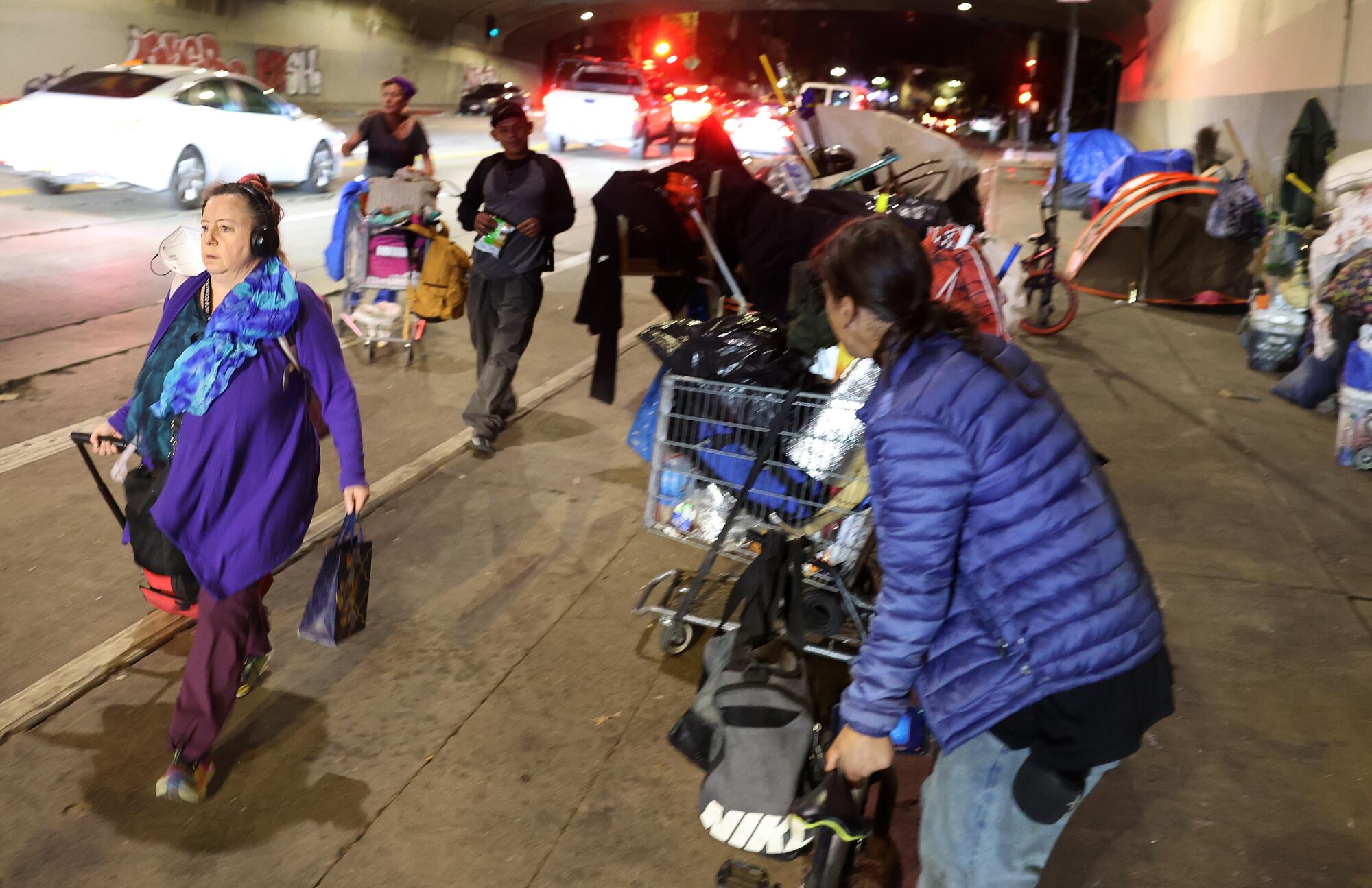 A pedestrian walks by a homeless encampment under the 101 Freeway on Cahuenga Boulevard in Hollywood.