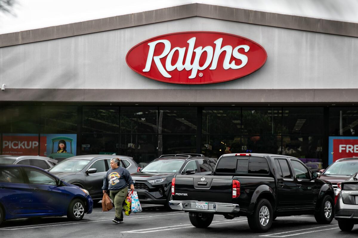 A man walks in the parking lot of a grocery store while holding grocery bags