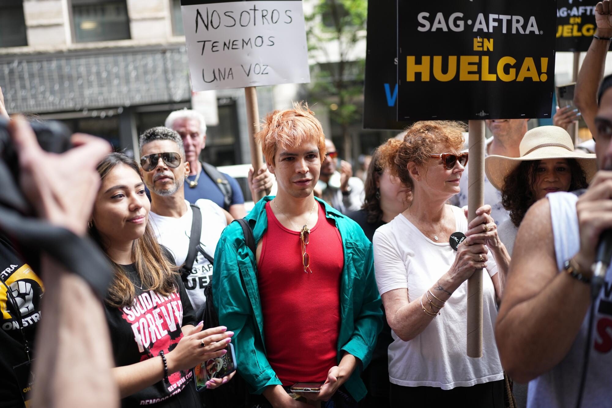 An actor wearing a bright red tank top is seen on the picket line with other performers on strike.