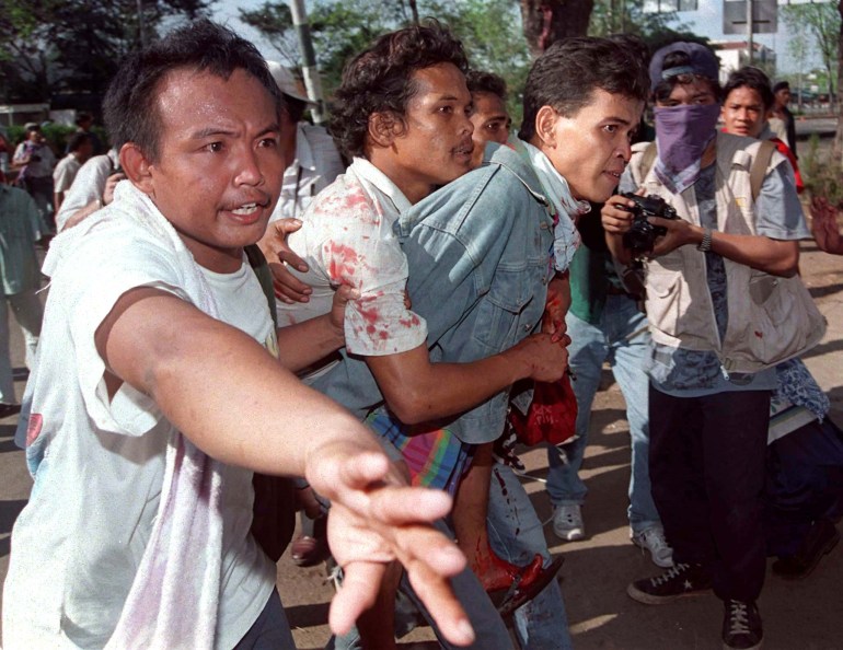 Students carrying an injured Trisakti protester to safety. The injured man has blood on his clothing and is on the back of another protester