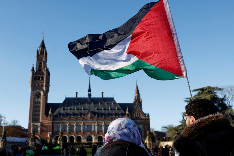 people wave a palestinian flag outside an old building with a tower