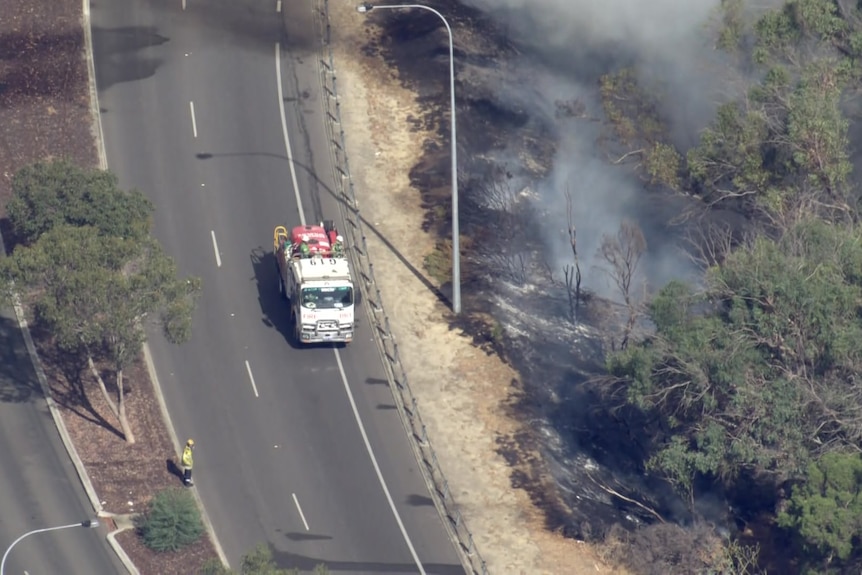 A fire truck on a road near burnt ground. 