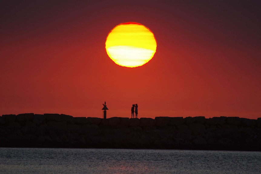 Two people in silhouette watching sunset from rocks