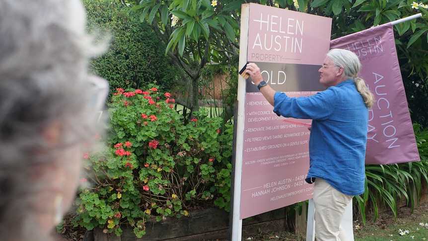 A man stick a sold sign on an auction board outside a house.