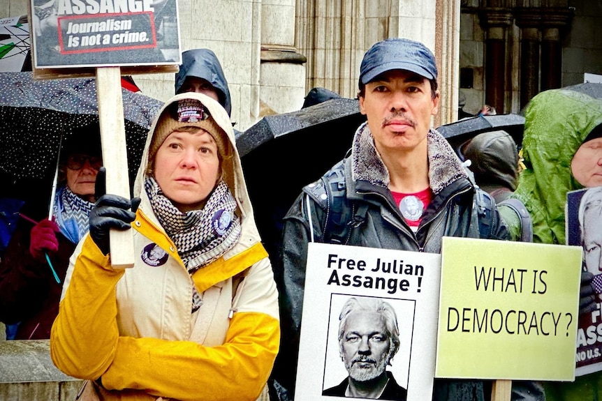 Two people with neutral expressions, holding signs, outside an old building