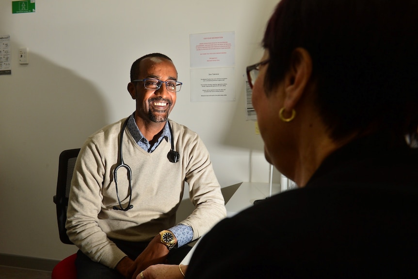 A doctor with a stethoscope around his neck talks to patient