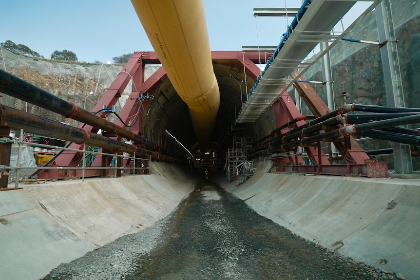 The entrance to a tunnel with a concrete floor, surrouned by industrial equipment. 