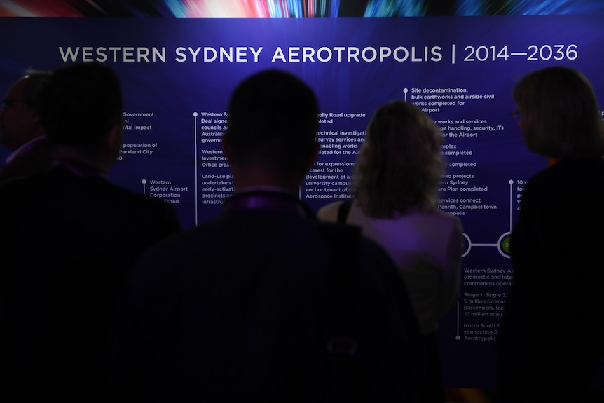 People seen from behind stand in front of a board headlined "Westers Sydney Aerotropolis".