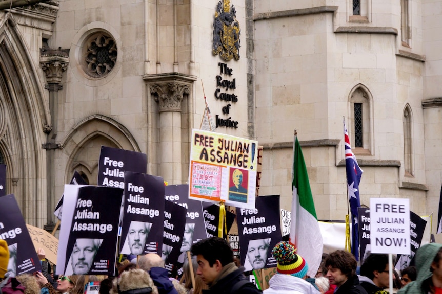 A large crowd of people holding signs with supportive slogans of Julian Assange