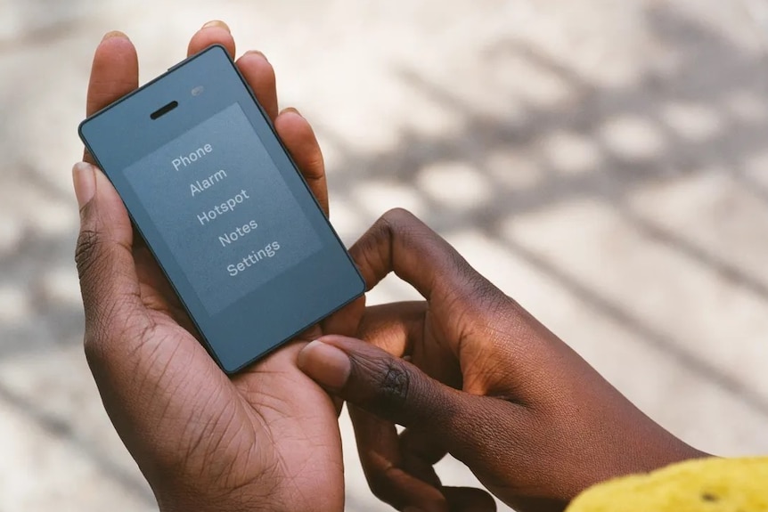 A close up of a pair of hands holding a Light Phone II outdoors.