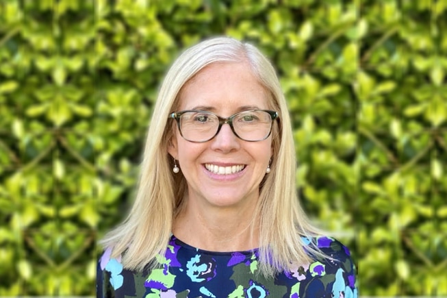 A blonde woman with glasses and a pattern shirt smiles