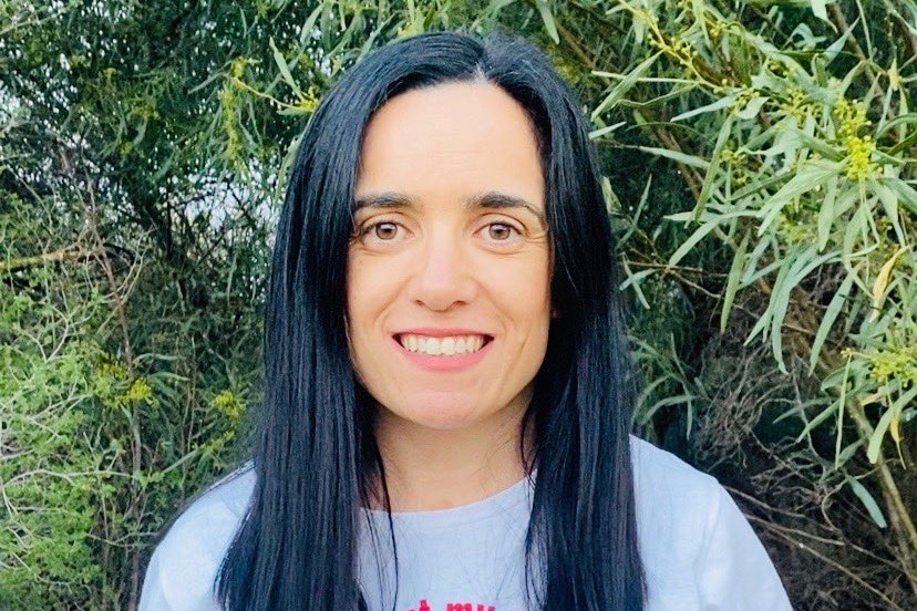 A woman with long black hair and a white tshirt smiles at the camera