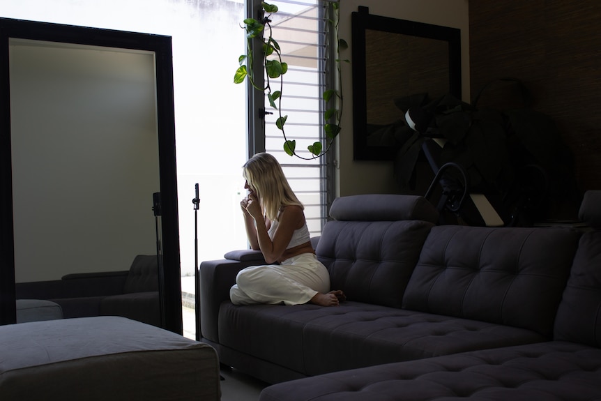 A young woman sits on a couch in front of a phone on a stand.