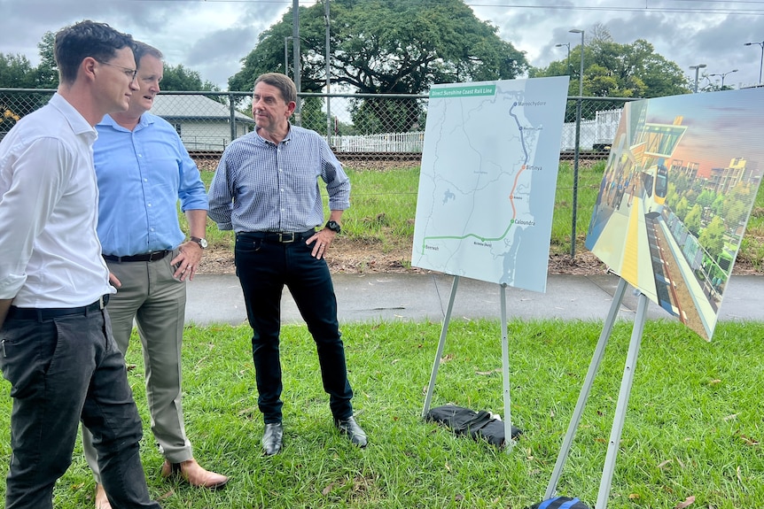 Three male politicians look at a map of the new Sunshine Coast rail line.