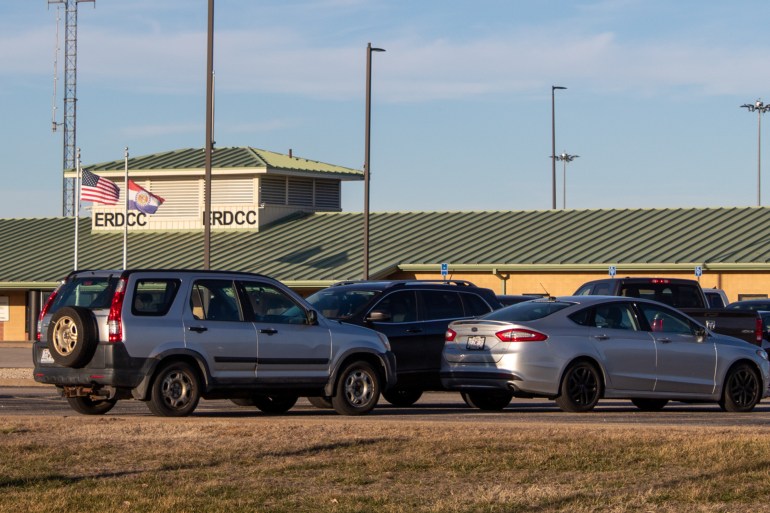 Cars can be seen parked in front of a single storey prison with a green tiled roof.