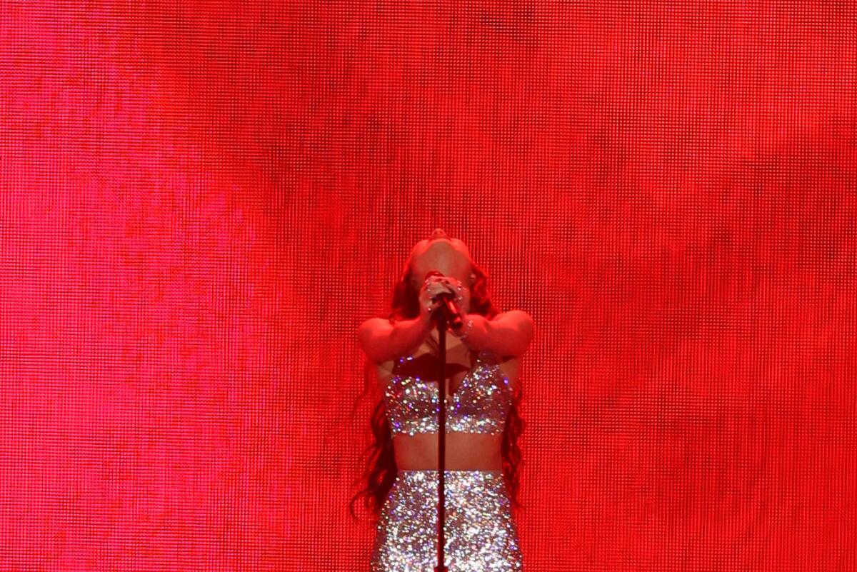 Olivia Rodrigo leans her head back while holding a microphone stand in front of a red backdrop.