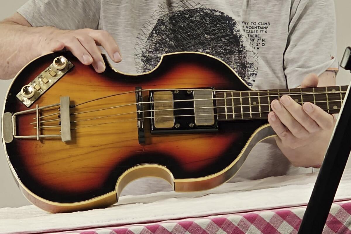 Torso of a person in a gray shirt holding the body of a wooden guitar