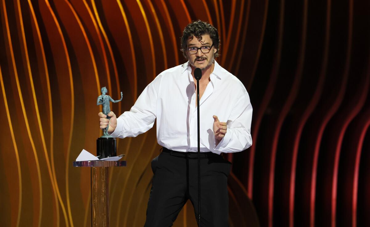 A surprised man in a white shirt accepts an acting honor.