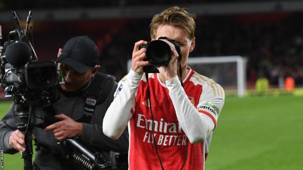 Martin Odegaard celebrates by using a club photographer's camera after Arsenal's win over Liverpool