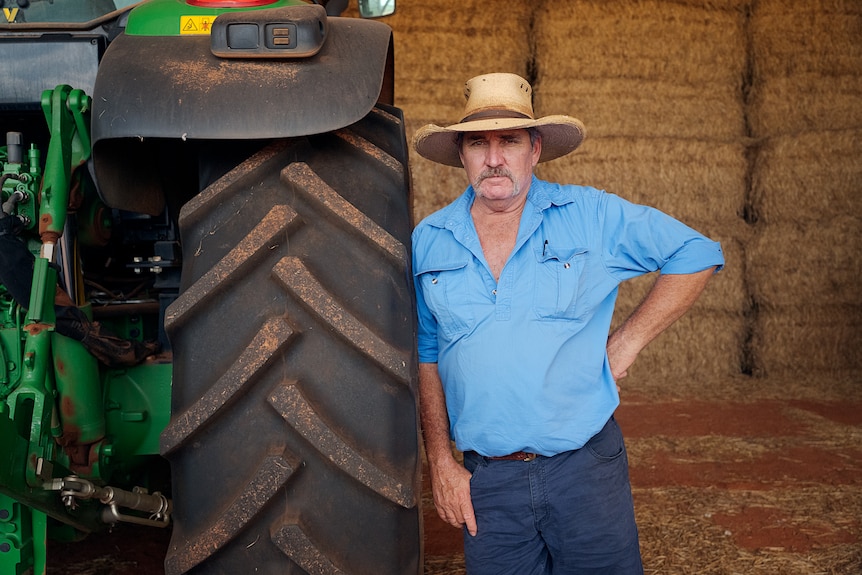 Man in blue shirt and hat standing next to bulldozer.