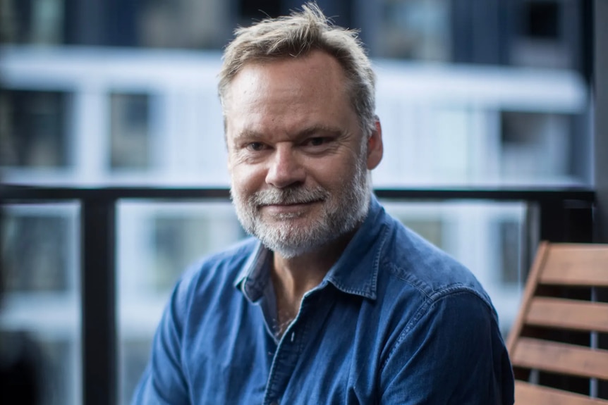 Robbie Egan with grey hair and beard, warm expression, blue shirt the shade of denim