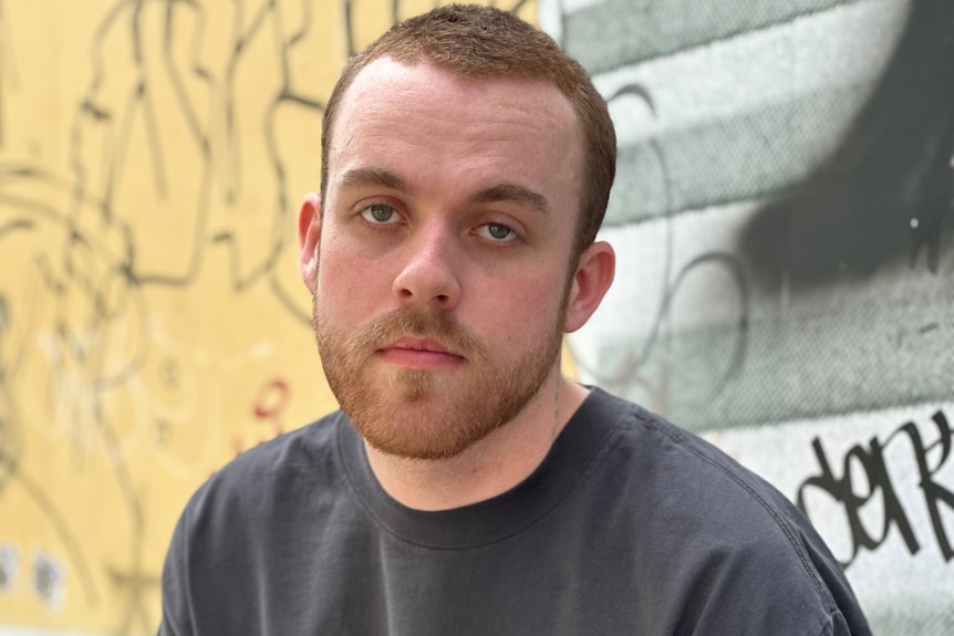 A man sits on an outdoor wall looking serious.