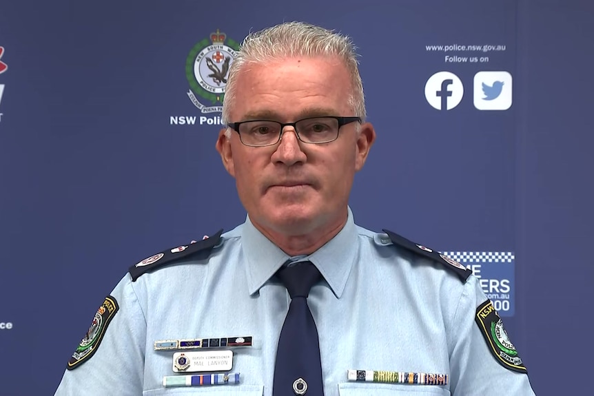 A man in a police uniform wearing glasses speaks to the media.