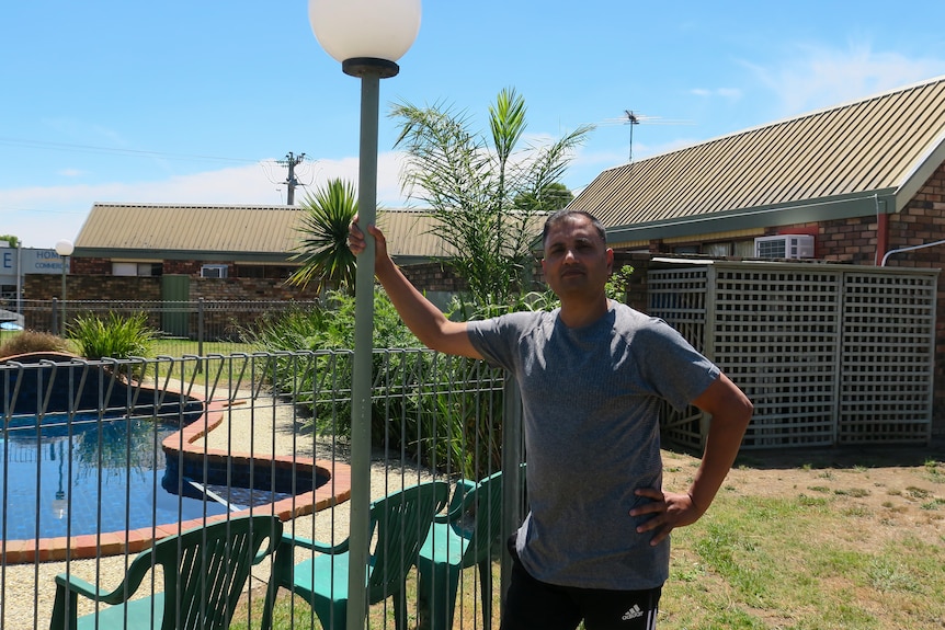 A man in a t-shirt holding a light pole next to a swimming pool