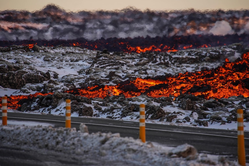 orange lava mixed with black rock and white snow covering the side of a road