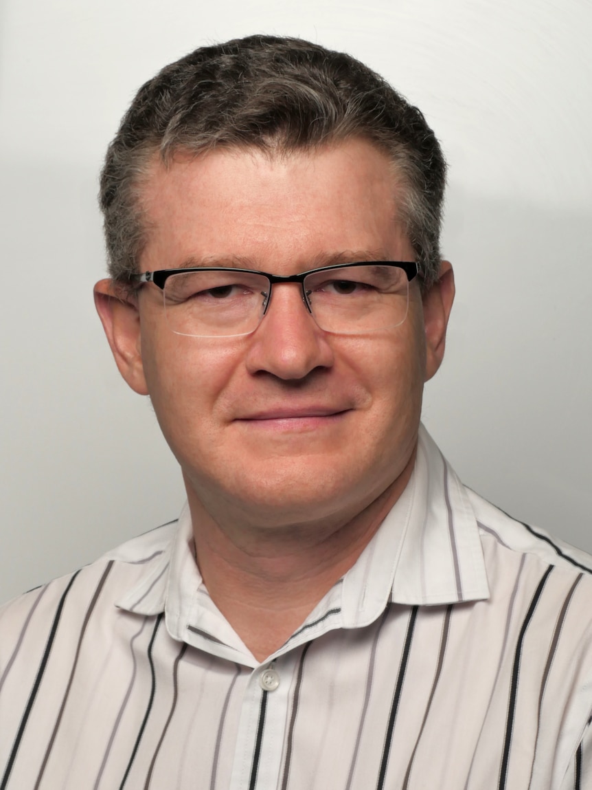 A headshot of a man wearing glasses and a striped shirt