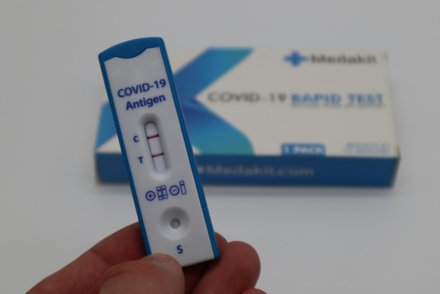 a positive covid test in someone's hand, with the box behind it