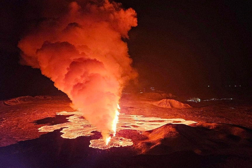 A bright orange smoke cloud rising from bright orange lava in a upside down triangle shape against a dark black sky