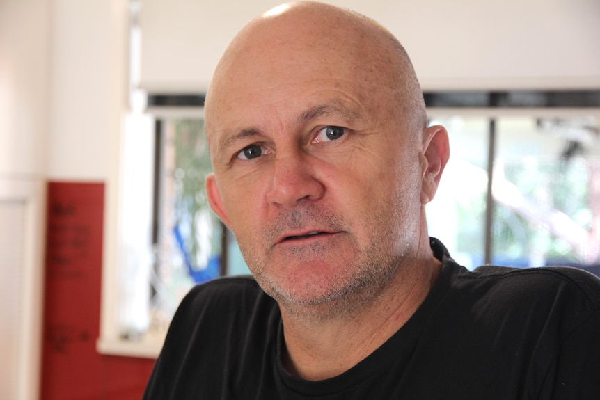 Bald man with dark eyes, well lit window behind him