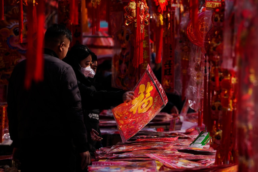 A couple wearing face masks picking out red decorations from a stall