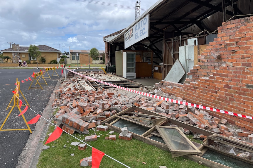 Bricks and windows on the ground, a red tape around it, sky scattered with clouds, houses in the distance.