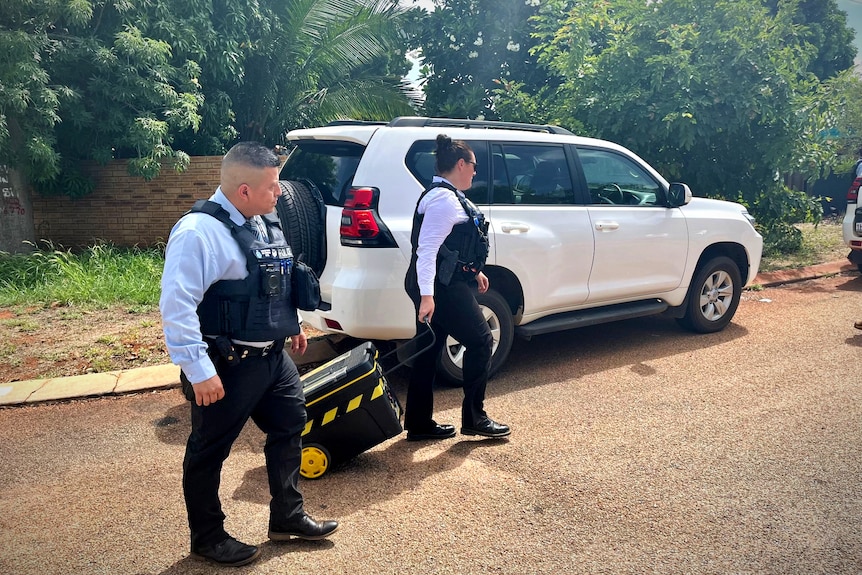 Police remove a black and yellow suitcase from a home