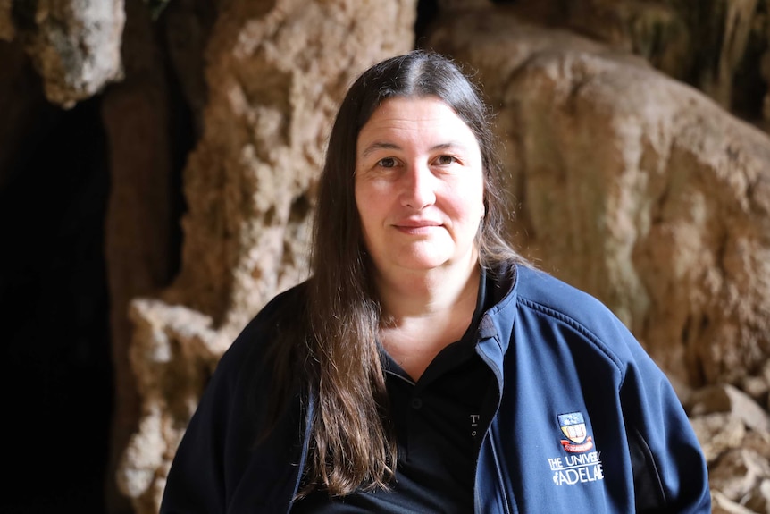 A woman wearing a University of Adelaide jacket stands in a cave